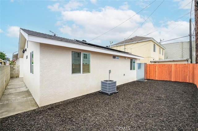 back of house with stucco siding, central AC unit, a fenced backyard, and roof mounted solar panels
