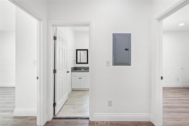 hallway featuring baseboards, light wood-style flooring, a sink, and electric panel