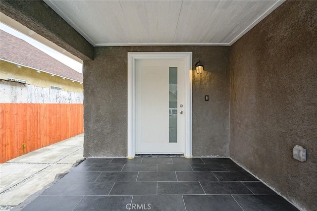 view of exterior entry with stucco siding, fence, and a patio
