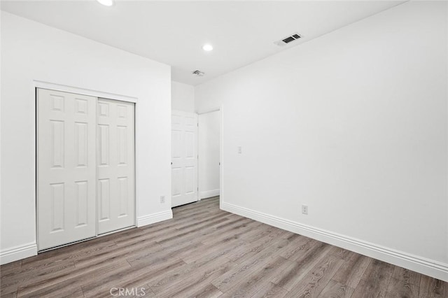 unfurnished bedroom featuring a closet, wood finished floors, baseboards, visible vents, and recessed lighting