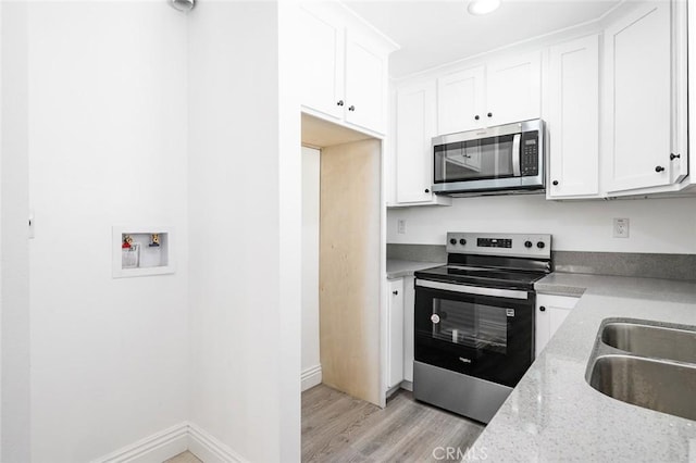 kitchen with light stone counters, a sink, white cabinetry, appliances with stainless steel finishes, and light wood-style floors