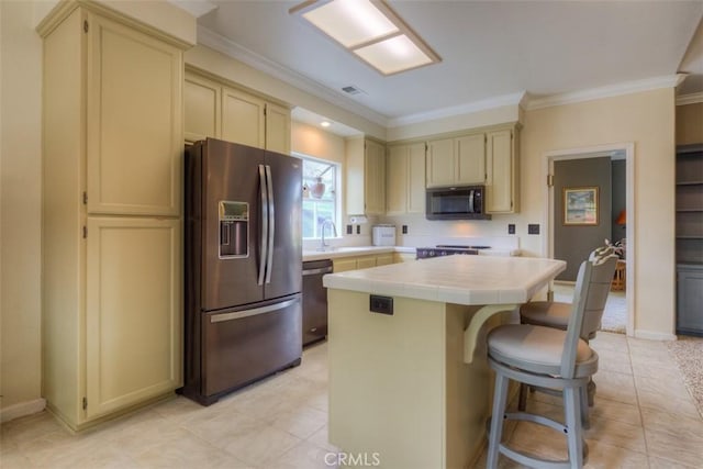 kitchen featuring tile counters, cream cabinetry, crown molding, a center island, and appliances with stainless steel finishes