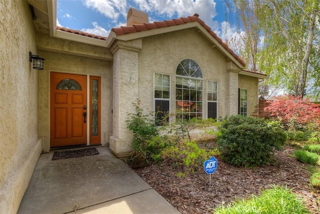 entrance to property featuring a chimney, stucco siding, and a tile roof