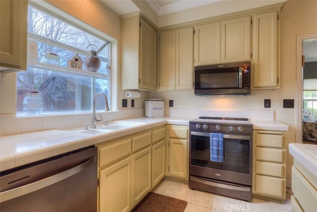 kitchen featuring tile counters, light tile patterned floors, stainless steel appliances, and a sink