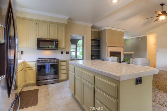 kitchen featuring stainless steel electric range oven, a multi sided fireplace, black fridge, a ceiling fan, and tile countertops