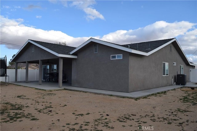 rear view of house featuring fence, a patio, a trampoline, stucco siding, and cooling unit