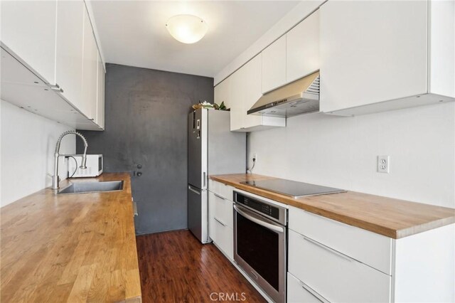kitchen with a sink, stainless steel oven, black electric stovetop, wood counters, and under cabinet range hood