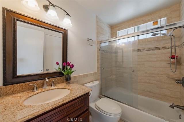 full bath with enclosed tub / shower combo, toilet, vanity, and tile walls