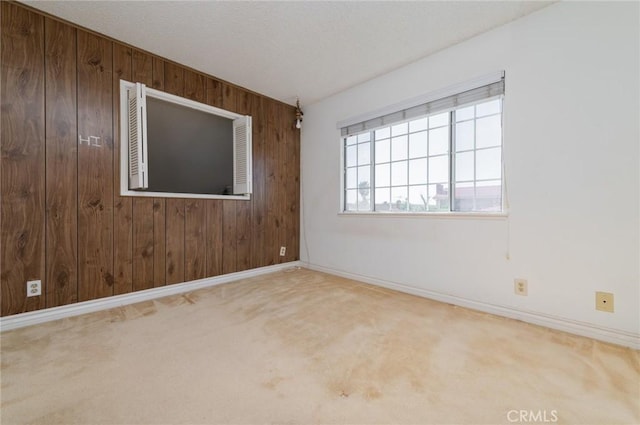 carpeted spare room with baseboards, wood walls, and a textured ceiling