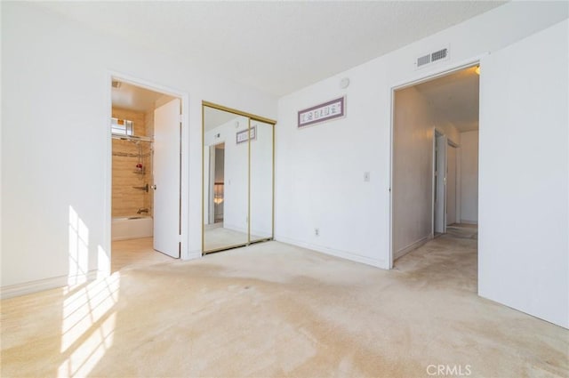 unfurnished bedroom with a closet, carpet flooring, visible vents, and ensuite bath