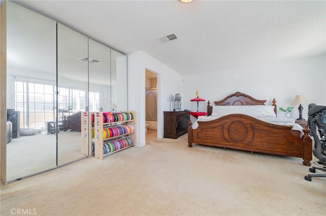 bedroom featuring ensuite bath, a textured ceiling, visible vents, and carpet