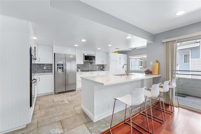23163 Mulholland Dr Unit 6, Woodland Hills, CA 91364 - kitchen featuring appliances with stainless steel finishes, tasteful backsplash, a kitchen bar, white cabinets, and recessed lighting