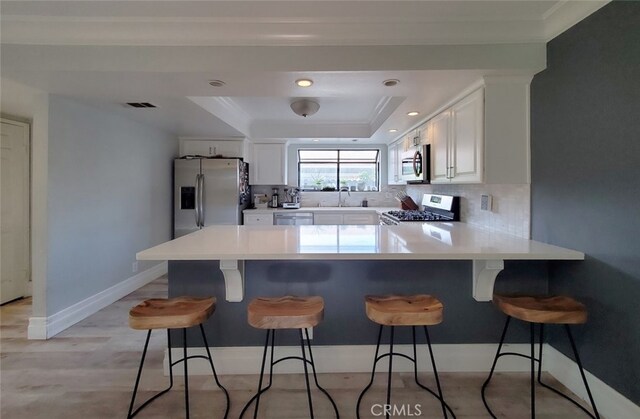 2512 Santa Ana Ave Unit 9, Costa Mesa, CA 92627 - kitchen with appliances with stainless steel finishes, a tray ceiling, a peninsula, white cabinetry, and ornamental molding