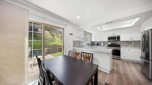 dining area featuring light wood finished floors, visible vents, recessed lighting, and a raised ceiling