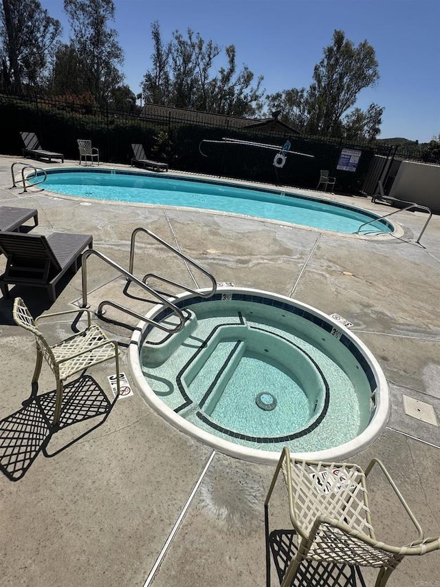 pool with fence, a hot tub, and a patio