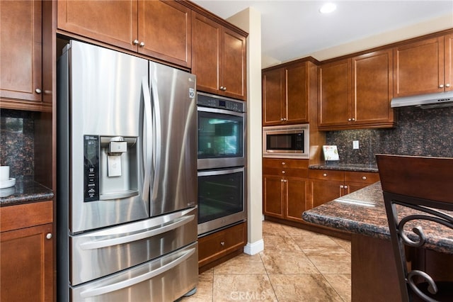 34595 Collier Falls Ct, Temecula, CA 92592 - kitchen with appliances with stainless steel finishes, under cabinet range hood, tasteful backsplash, dark stone countertops, and light tile patterned floors