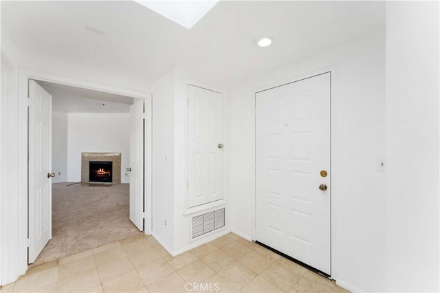 foyer entrance with light carpet, a fireplace with flush hearth, baseboards, visible vents, and recessed lighting