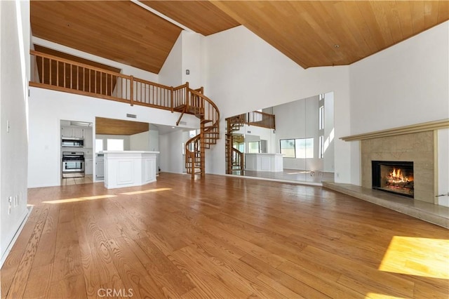 unfurnished living room with stairs, high vaulted ceiling, wood ceiling, a fireplace, and wood finished floors