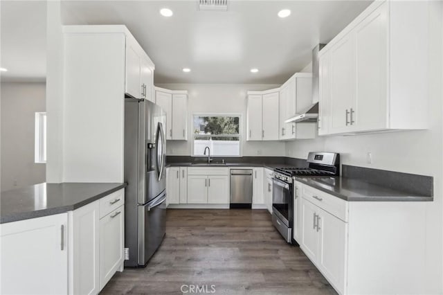 kitchen featuring recessed lighting, range hood, stainless steel appliances, dark countertops, and white cabinets