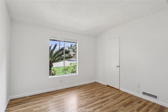spare room with wood finished floors, visible vents, baseboards, and a textured ceiling