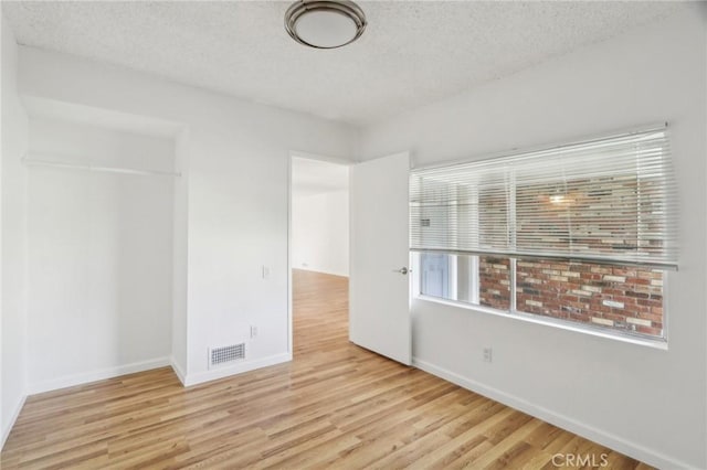 unfurnished bedroom with a textured ceiling, visible vents, wood finished floors, and baseboards