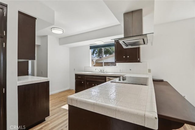 kitchen featuring black electric stovetop, dark brown cabinetry, light wood-style flooring, a peninsula, and island range hood