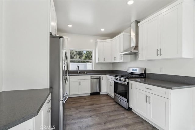 kitchen with appliances with stainless steel finishes, a sink, dark countertops, and wall chimney exhaust hood