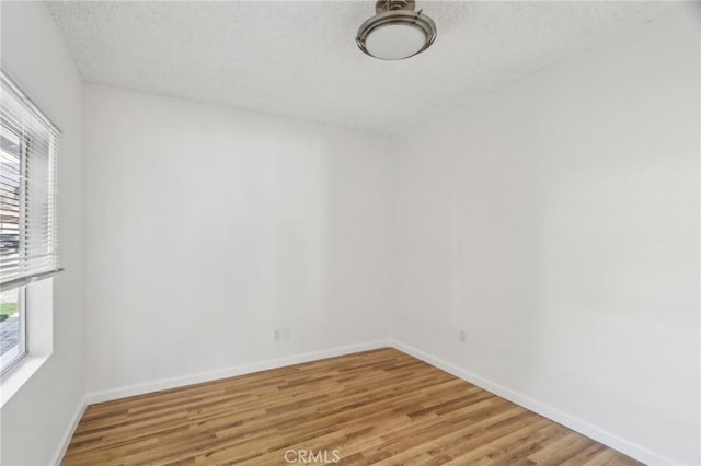 unfurnished room featuring a textured ceiling, light wood-style flooring, and baseboards