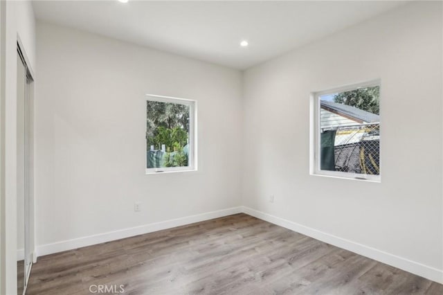 unfurnished room featuring baseboards, recessed lighting, wood finished floors, and a healthy amount of sunlight