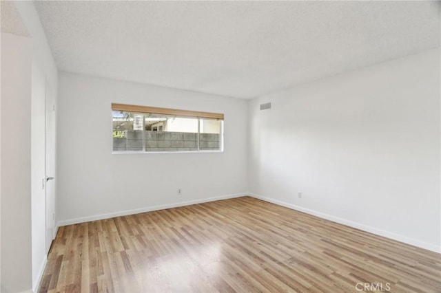 unfurnished room with baseboards, visible vents, wood finished floors, and a textured ceiling