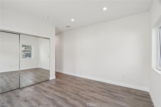 unfurnished bedroom with baseboards, recessed lighting, wood finished floors, and a closet