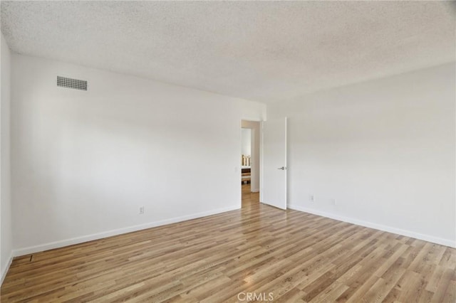 empty room with a textured ceiling, visible vents, baseboards, and light wood-type flooring