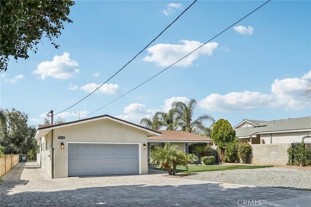 ranch-style house with fence, decorative driveway, stucco siding, and an attached garage