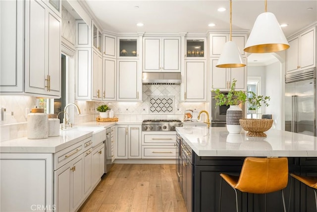 2107 Lemon Heights Dr, Santa Ana, CA 92705 - kitchen featuring an island with sink, light wood-style flooring, backsplash, appliances with stainless steel finishes, and hanging light fixtures