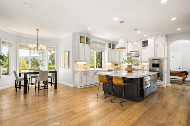 2107 Lemon Heights Dr, Santa Ana, CA 92705 - kitchen featuring wall chimney exhaust hood, arched walkways, a center island, appliances with stainless steel finishes, and light countertops