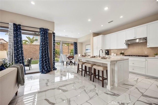 kitchen featuring decorative backsplash, white cabinetry, a kitchen breakfast bar, and under cabinet range hood