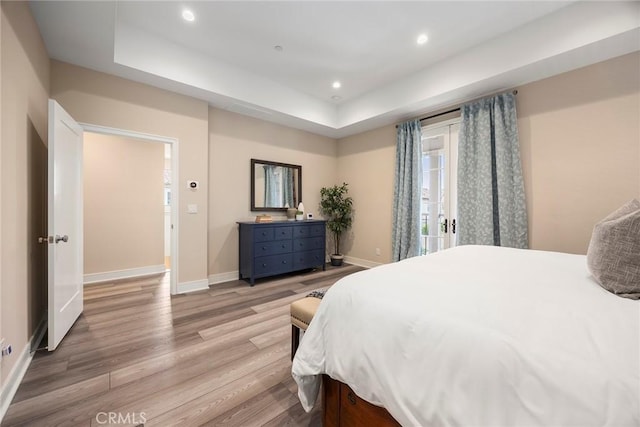bedroom with a raised ceiling, light wood finished floors, baseboards, and multiple windows