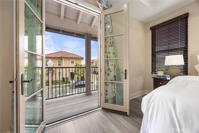 bedroom with access to outside, baseboards, beamed ceiling, and wood finished floors