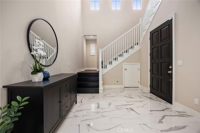 foyer with baseboards, stairway, marble finish floor, and a high ceiling