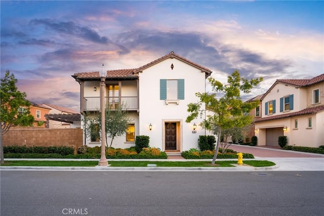 mediterranean / spanish-style house featuring an attached garage, a tile roof, fence, stucco siding, and a balcony