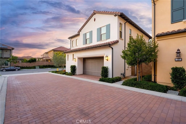 mediterranean / spanish-style home with a tiled roof, a garage, decorative driveway, and stucco siding