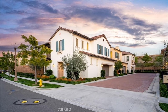 view of front of house featuring an attached garage, a tiled roof, stucco siding, and decorative driveway