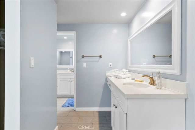 full bath featuring baseboards, a sink, recessed lighting, and two vanities