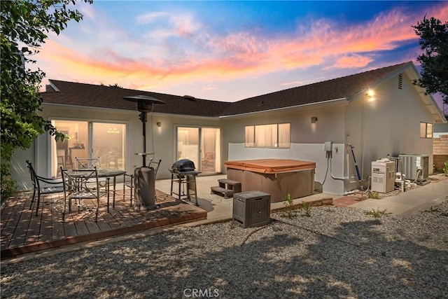 back of property at dusk with a hot tub, central AC unit, ac unit, and stucco siding