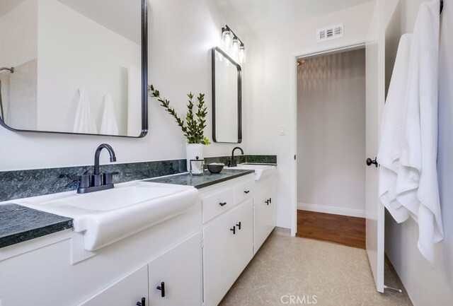 bathroom featuring a sink, visible vents, baseboards, and double vanity