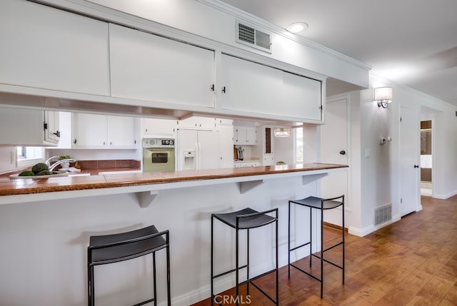 kitchen with a peninsula, white appliances, visible vents, and light wood-type flooring