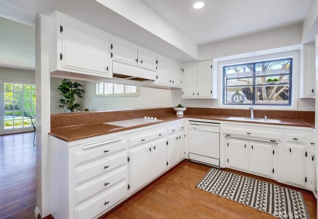 kitchen with light wood-style floors, white appliances, white cabinets, a sink, and dark countertops