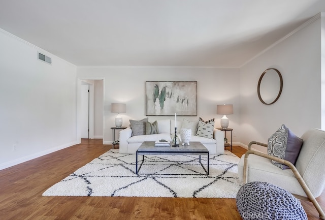 living room with crown molding, visible vents, baseboards, and wood finished floors