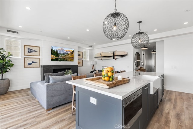 kitchen with a kitchen island with sink, a sink, visible vents, recessed lighting, and light wood-style floors