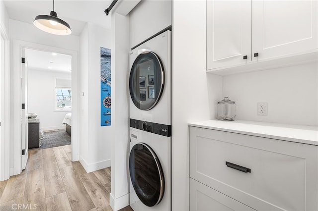 clothes washing area featuring baseboards, stacked washing maching and dryer, laundry area, and light wood-type flooring